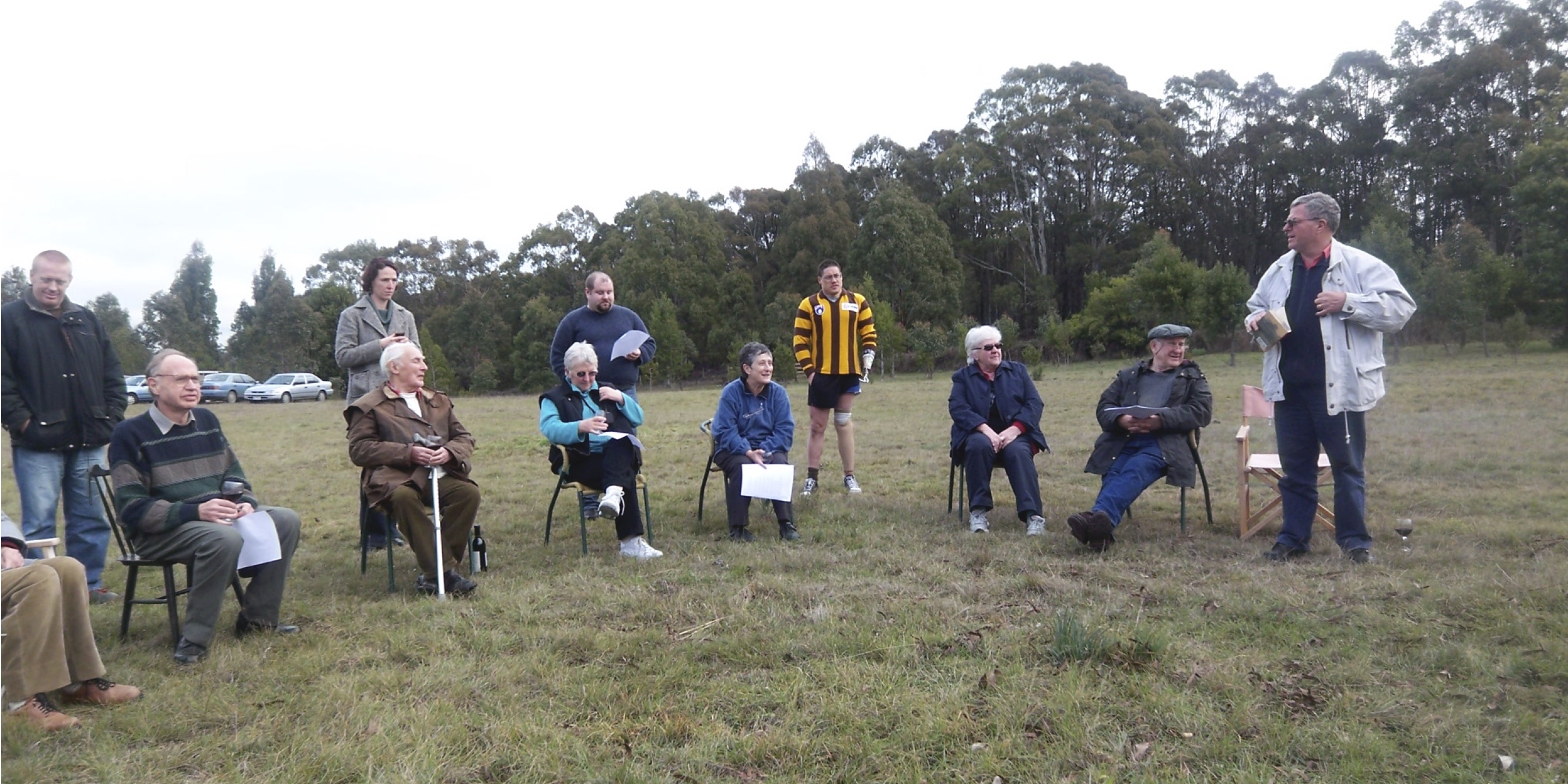Dr Chris Watson standing on right of a group of friends expounding on poetry. Dr Val Noone to his right.